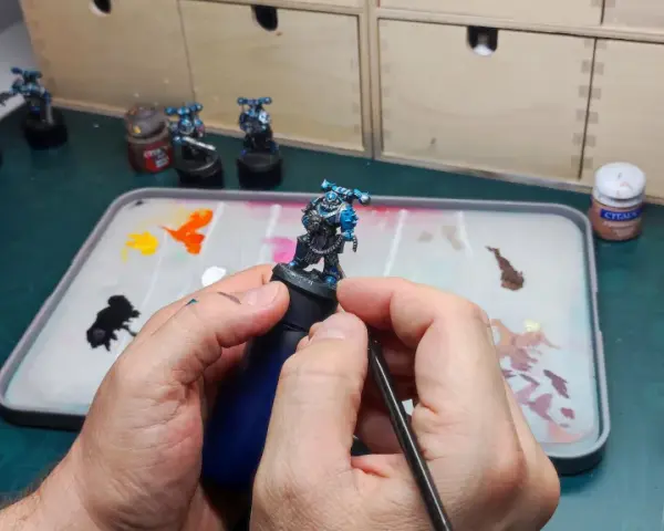 Mani che dipingono miniature, con pennello e tavolozza piena di colori.