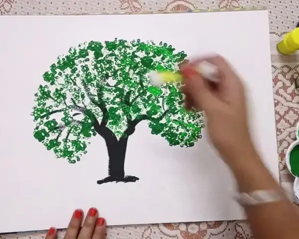 Mano che dipinge alberi con cotton fioc, creando un effetto di fogliame con tanti piccoli cerchi verdi.