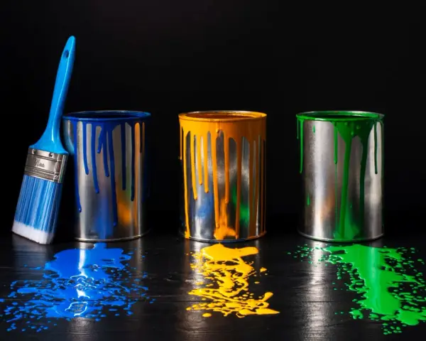 Tre barattoli di vernice blu, gialla e verde gocciolano su un tavolo di legno scuro. Un pennello blu è appoggiato al barattolo blu. Un'alternativa all'alcool isopropilico per pulire?