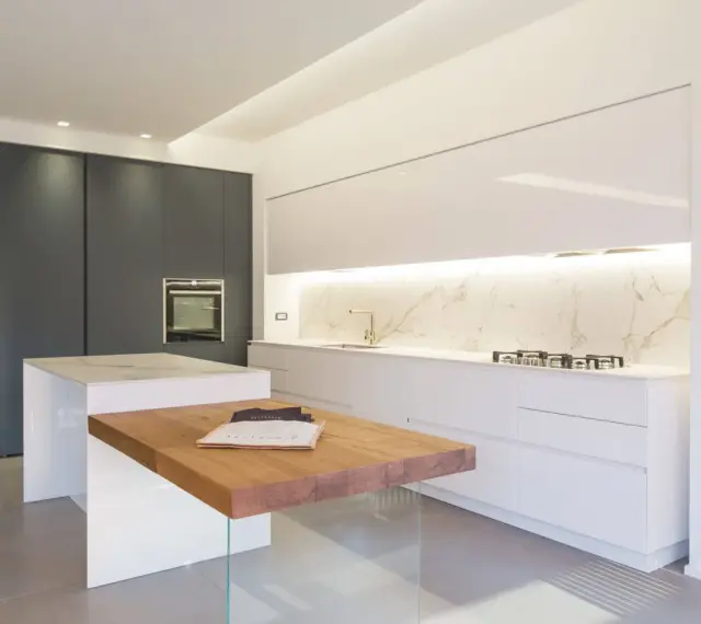 Cucina moderna con isola centrale in legno e marmo. Mobili bianchi lucidi e un piano in marmo creano eleganti sfumature di bianco, contrastando con le ante scure.