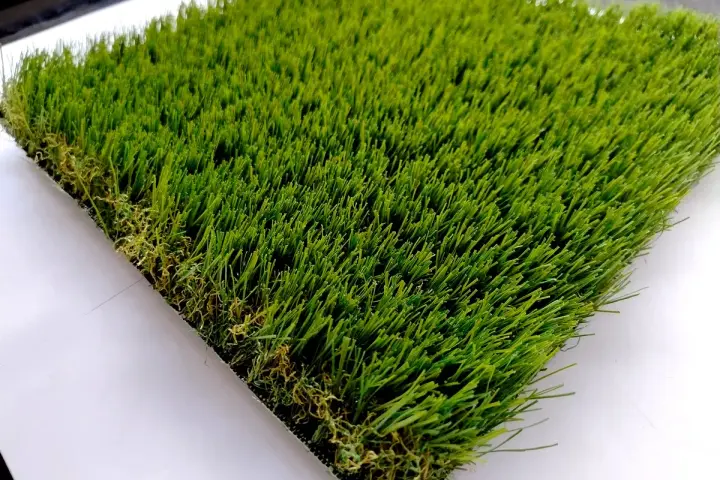 Un campione di erba sintetica, verde brillante e folta, mostra come fare l'erba finta per un giardino perfetto.