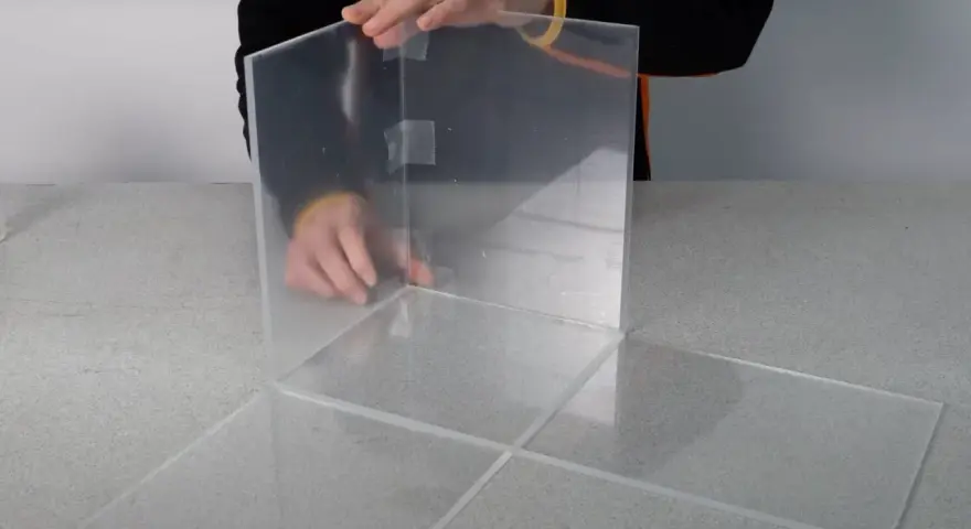 Costruzione di una teca in plexiglass fai da te, con pannelli trasparenti assemblati con nastro adesivo.