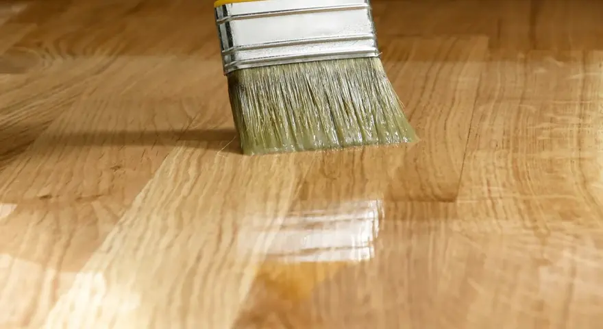 Pennello applica vernice lucida su parquet. La tabella gloss vernici mostra la brillantezza ottenuta.
