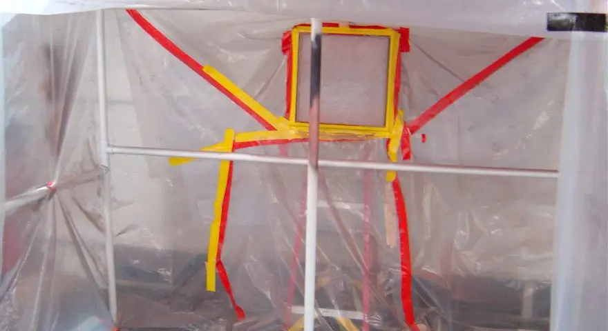 Struttura fai da te per verniciatura, con teli trasparenti e nastro giallo/rosso a delimitare l'area.
