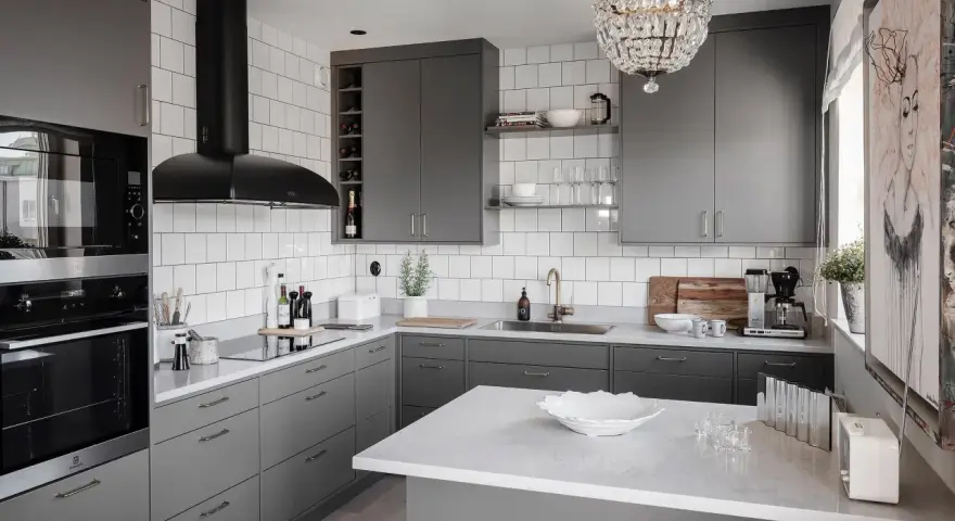Cucina moderna con mobili color titanio, cappa nera, piano in quarzo bianco e lampadario di cristallo.