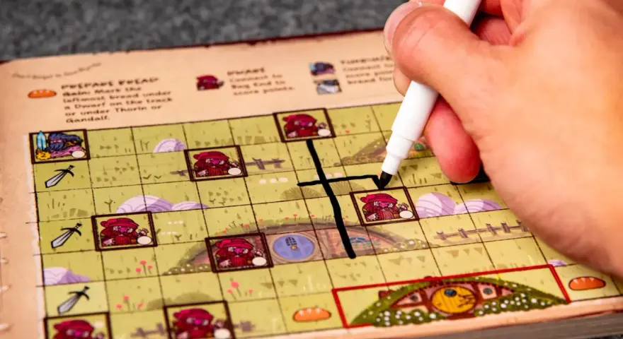 Mano che segna una casella su una plancia colorata, parte del gioco da tavolo "Hobbit il gioco".