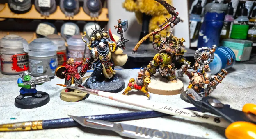 Miniature di Death Korps of Krieg e altri guerrieri pronti per la battaglia, circondati da colori e attrezzi per modellismo.