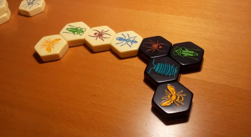 Pezzi esagonali del **hive gioco da tavolo** con insetti colorati disposti su un tavolo di legno.