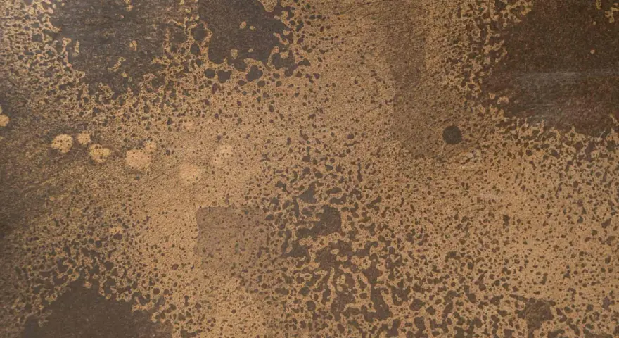 Superficie ruvida con macchie scure su sfondo dorato, che colore è il bronzo.