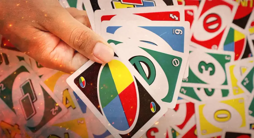 Mano che tiene carte UNO, pronte per una partita di "20 domande". Numeri, colori e simboli si mescolano in un gioco di strategia.