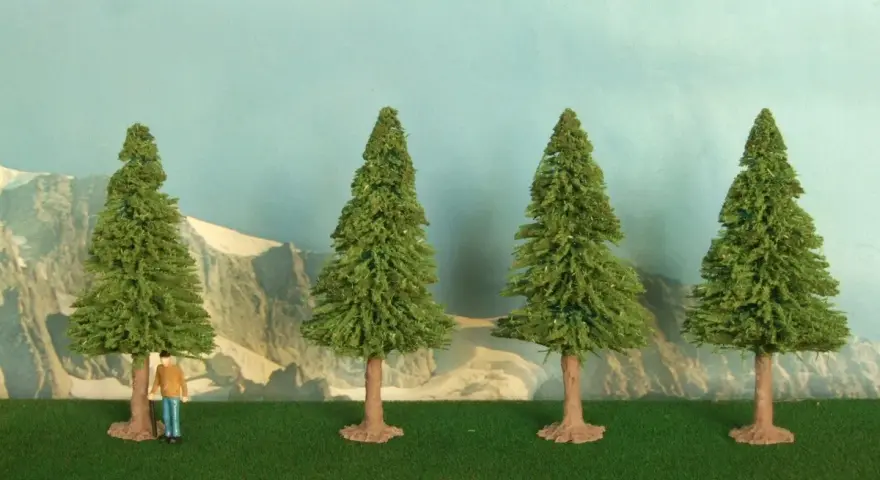 Un piccolo uomo osserva la scena, mentre si prova a costruire un albero finto. Quattro alberi verdi su un prato artificiale, con montagne sullo sfondo.