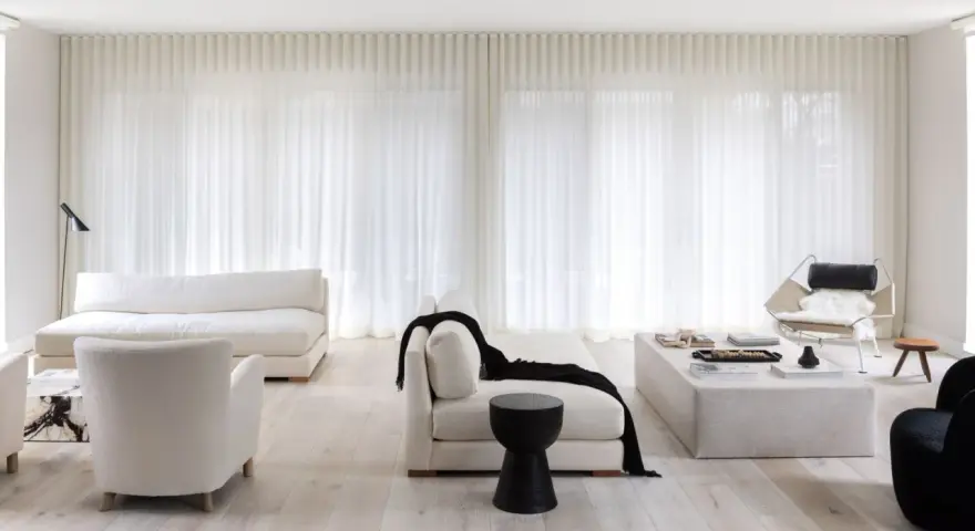 Soggiorno minimalista con divani bianchi, poltrone soffici e tende leggere. Un tocco di nero spezza la palette, creando 50 sfumature di bianco e contrasto.