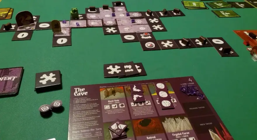 Vasto gioco da tavolo "The Cave" con tessere, carte e segnalini su un tappetino verde.