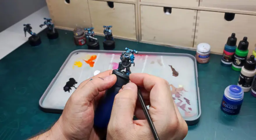 Mani che dipingono miniature, con pennello e tavolozza piena di colori.