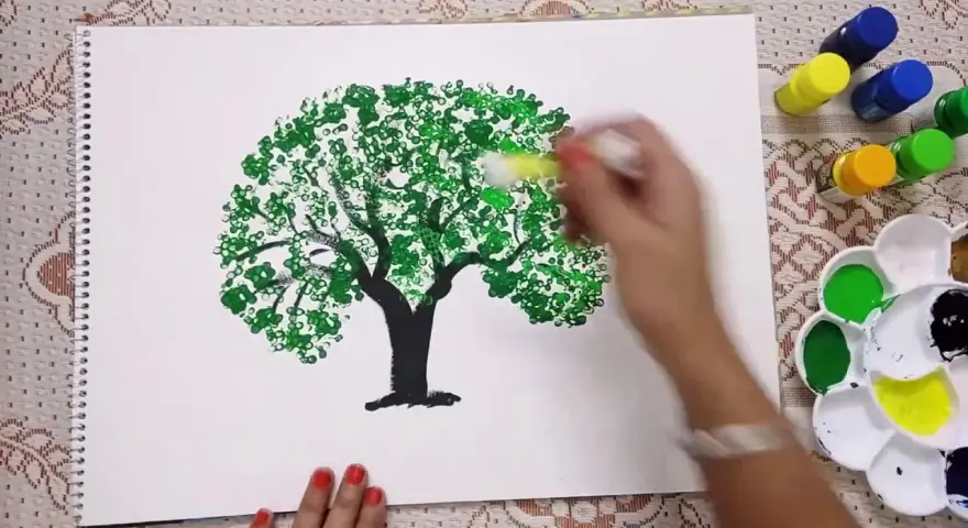 Mano che dipinge alberi con cotton fioc, creando un effetto di fogliame con tanti piccoli cerchi verdi.