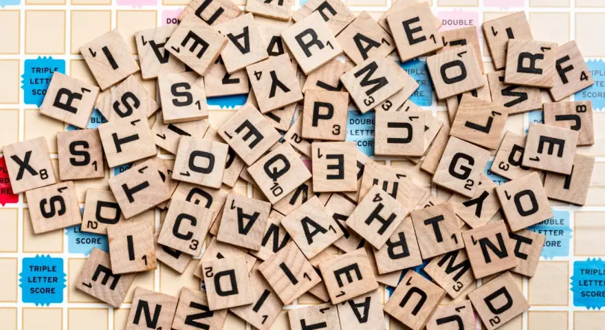 Un mucchio di tessere di Scarabeo sparse sul tabellone. Quante lettere si danno a Scarabeo per formare parole?