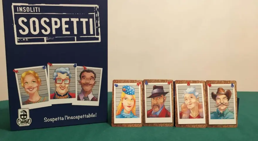 Il gioco "Insoliti Sospetti" presenta una scatola blu con ritratti di personaggi e carte con volti di sospetti, pronti per essere identificati.
