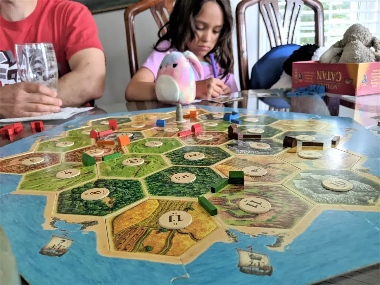 Una famiglia gioca a Catan, uno dei migliori giochi da tavolo, costruendo insediamenti su un'isola esagonale.