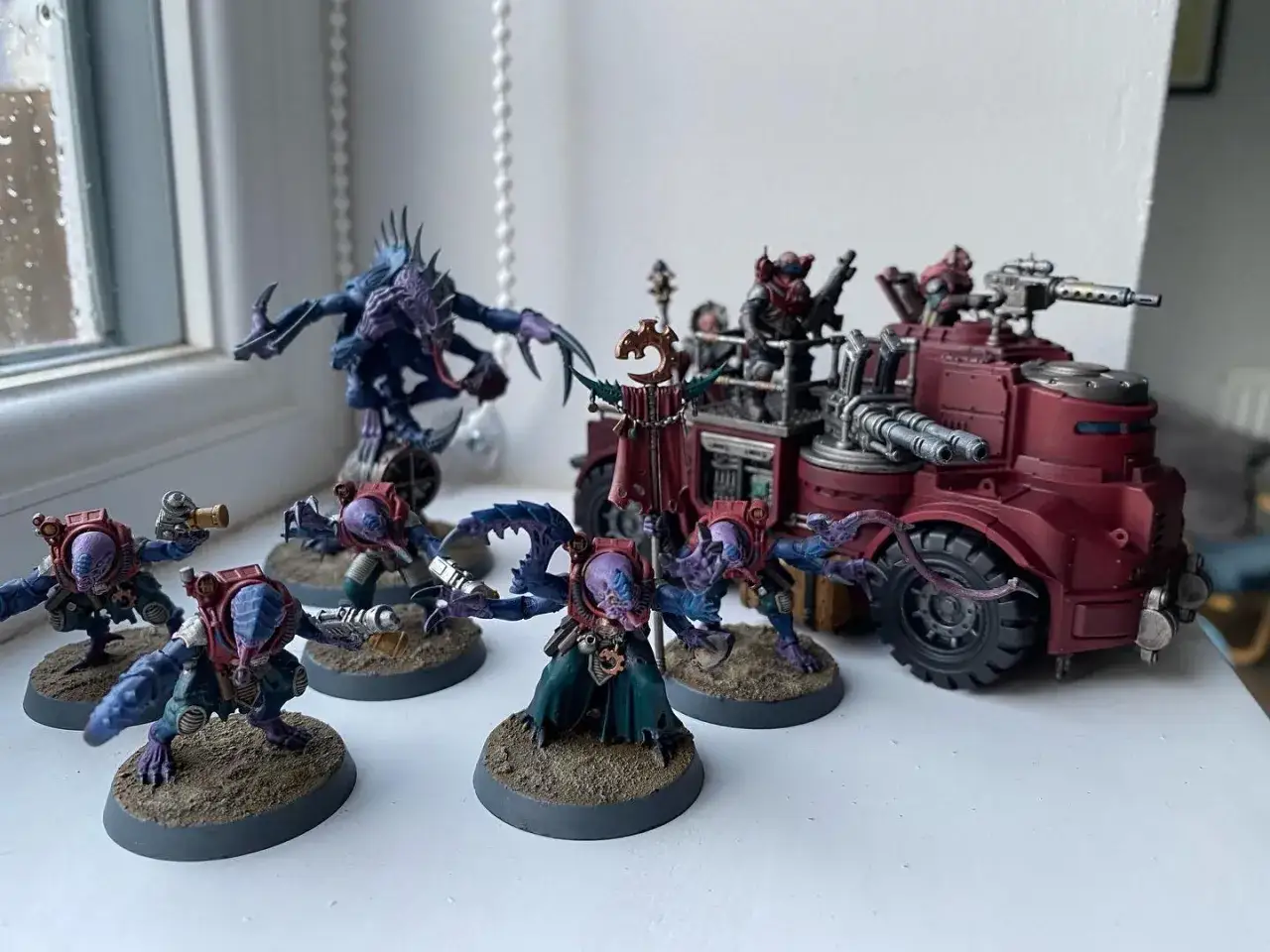 Un gruppo di miniature di un genestealer cult, con creature aliene e un veicolo rosso, pronti per la battaglia.