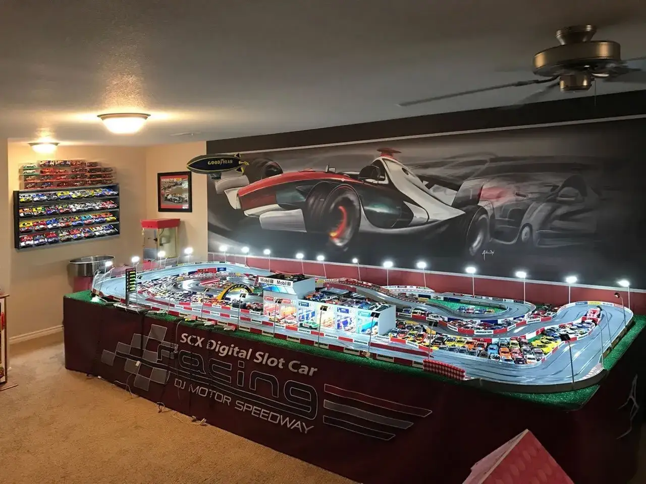 Scenografia di una pista per auto da corsa in miniatura, con una vasta collezione di modellini esposti su una parete. La tabella scala modellismo auto è dettagliata, con un circuito complesso e auto in gara.
