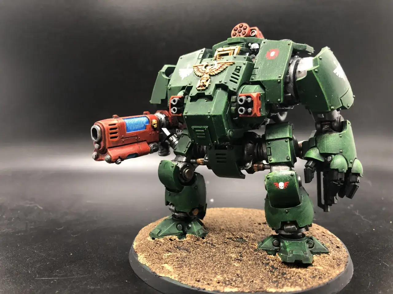 Un imponente Dreadnought verde, simbolo dei Dark Angels, pronto a combattere con il suo cannone rosso fiammante.