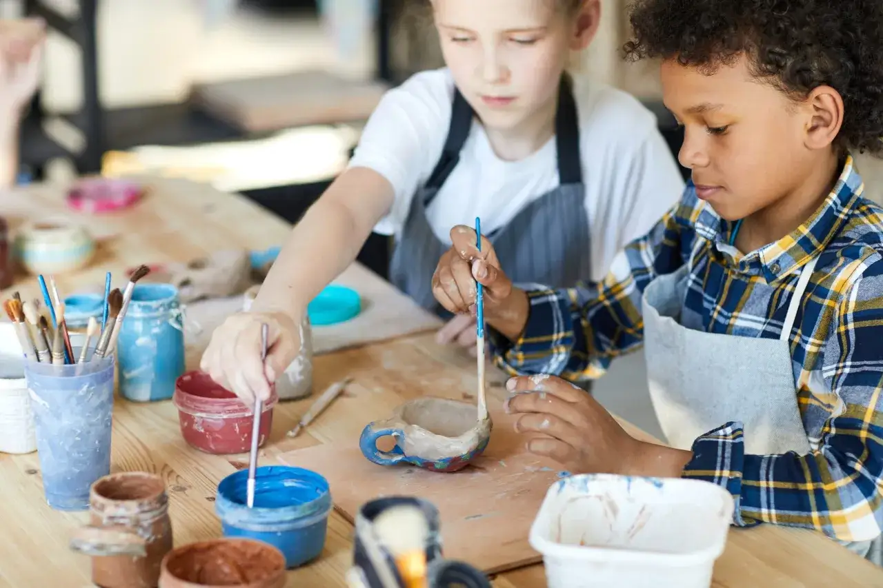 Bambini concentrati su come dipingere il das, creando piccole tazze di ceramica con colori vivaci.