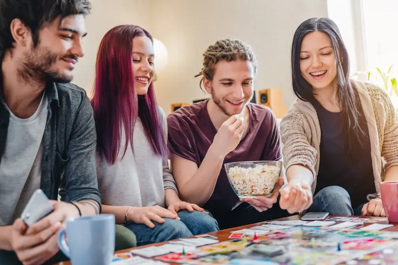 Amici che giocano a uno dei 10 giochi da tavolo per famiglie pi&ugrave; popolari, con popcorn e risate.