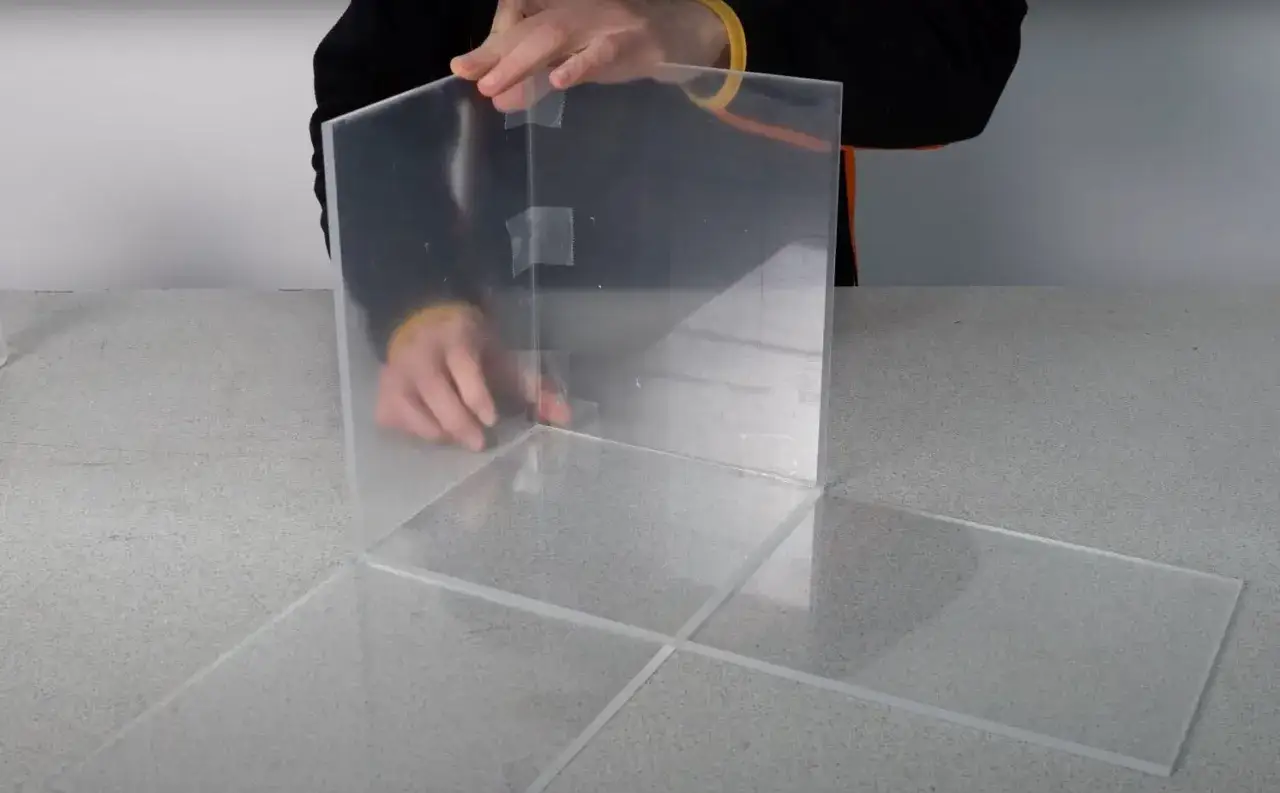 Costruzione di una teca in plexiglass fai da te. Pannelli trasparenti assemblati con nastro adesivo per creare una struttura.