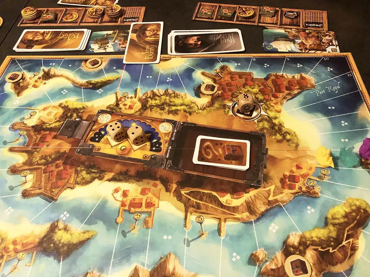 Il gioco da tavolo Port Royal con dadi, carte e pedine colorate su una mappa di isole e città.