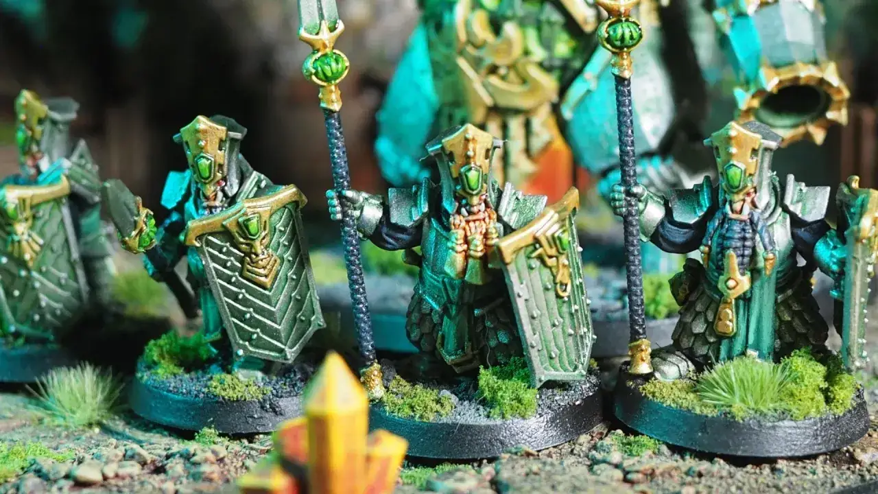Un gruppo di nani del caos, con armature verdi e oro, brandiscono lance e scudi, pronti alla battaglia.