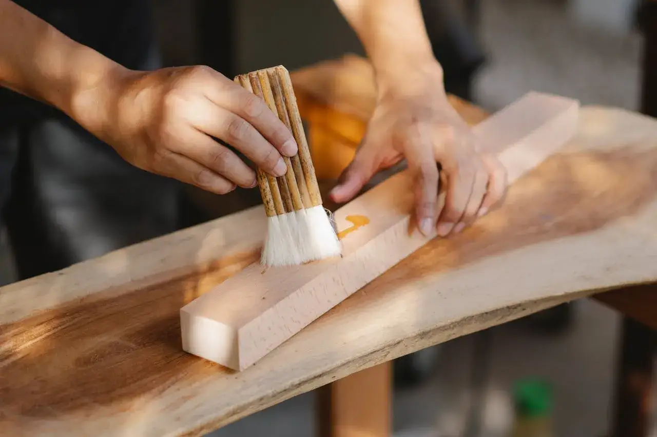Mani che applicano colla su legno con un pennello. Un metodo per rimuovere la colla Attak dal legno.