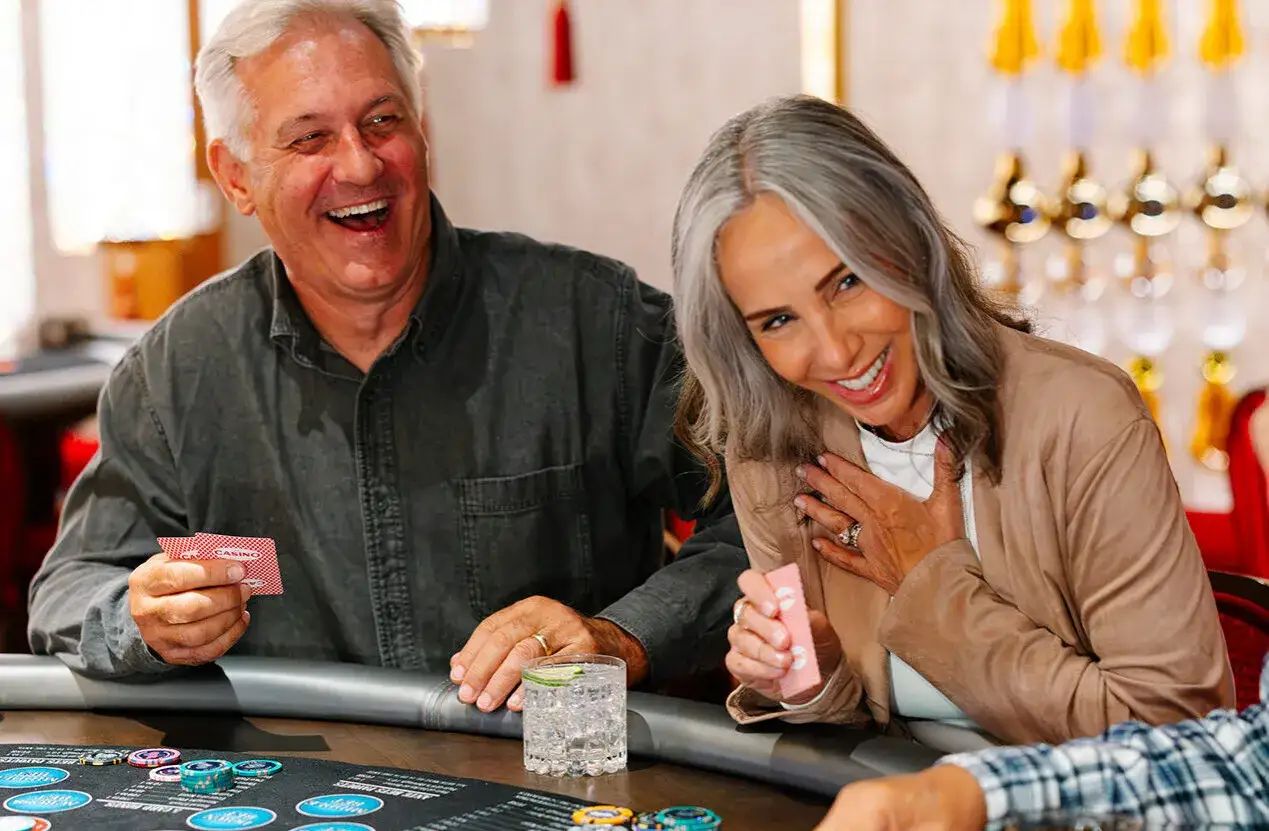 Coppia felice gioca a carte, divertendosi con giochi di carte da fare in due. Sul tavolo ci sono fiches e bicchieri.
