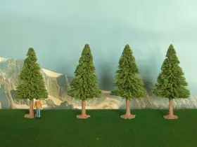 Un piccolo uomo osserva la scena, mentre si prova a costruire un albero finto. Quattro alberi verdi su un prato artificiale, con montagne sullo sfondo.