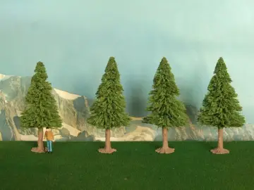 Un piccolo uomo osserva la scena, mentre si prova a costruire un albero finto. Quattro alberi verdi su un prato artificiale, con montagne sullo sfondo.