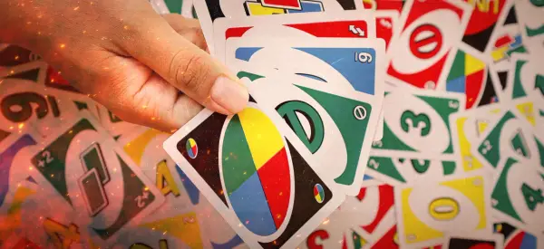 Mano che tiene carte UNO, pronte per una partita di "20 domande". Numeri, colori e simboli si mescolano in un gioco di strategia.