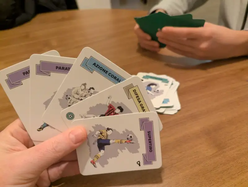 Mani che tengono carte da gioco con illustrazioni calcistiche, parte di giochi di carte da tavolo.