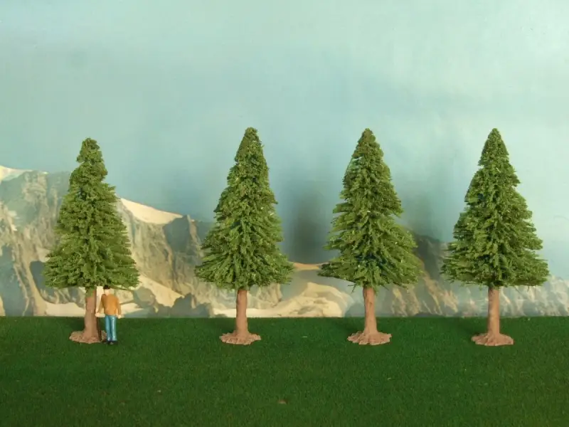 Un piccolo uomo osserva la scena, mentre si prova a costruire un albero finto. Quattro alberi verdi su un prato artificiale, con montagne sullo sfondo.
